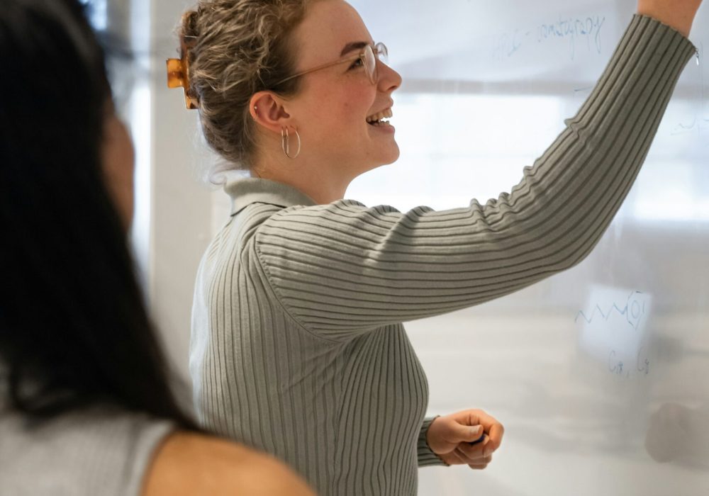Photo qui représente une femme souriante qui écrit sur un tableau.